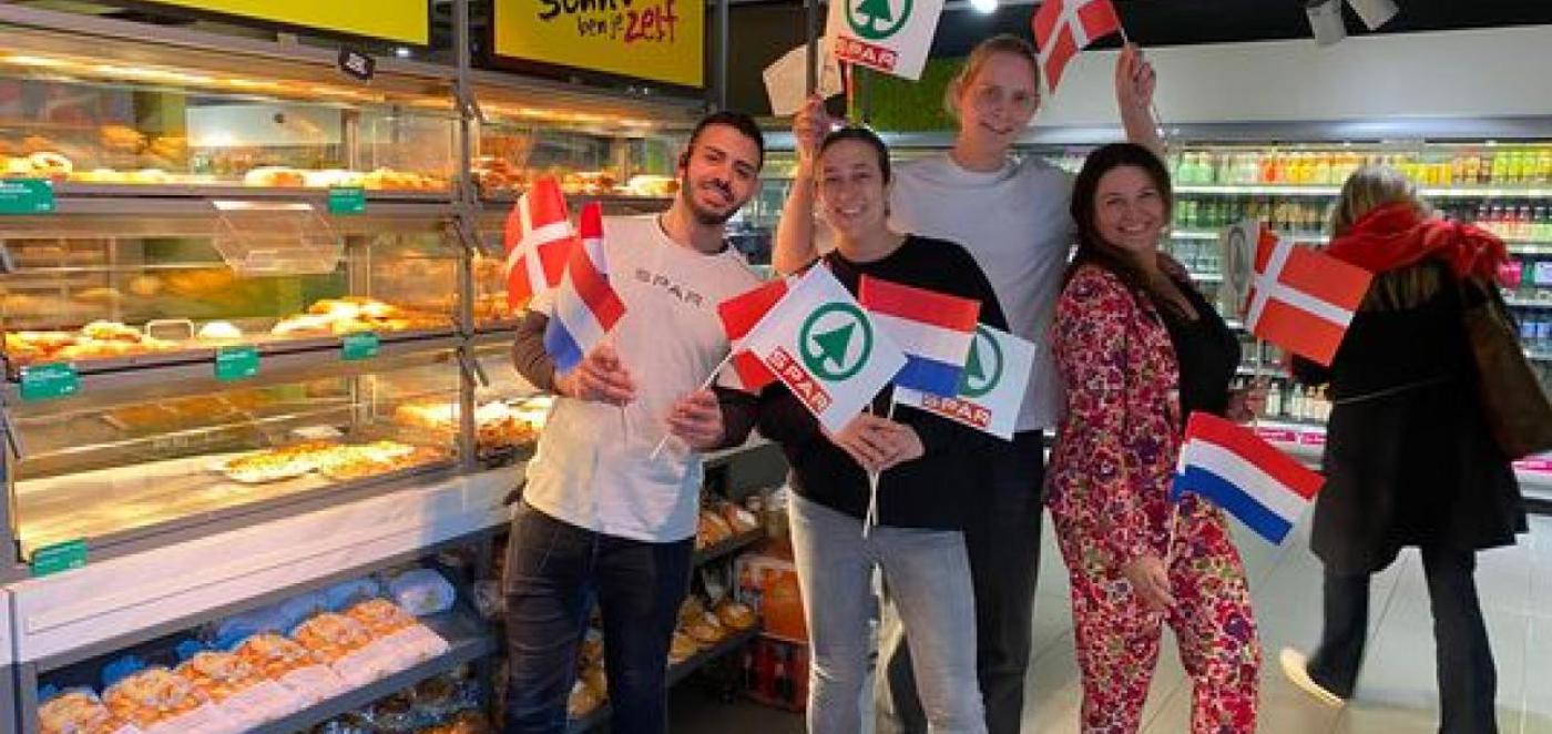 Fire personer holder danske og hollandske flag i et supermarked med bagværk i disken