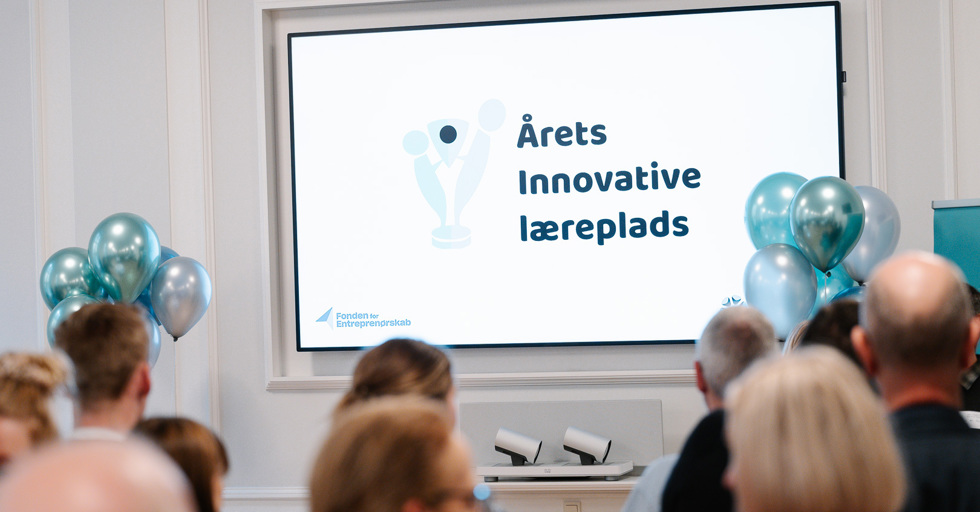 Skærm med teksten 'Årets Innovative læreplads' ved arrangement med balloner og publikum
