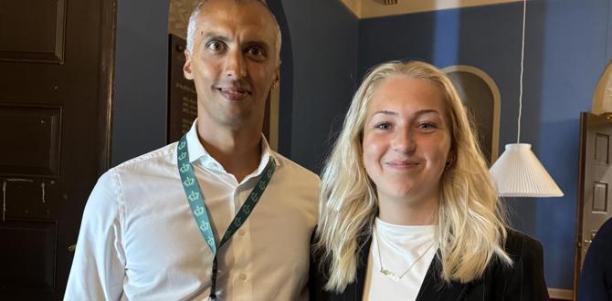 Mand i hvid skjorte med id-bånd og ung kvinde i sort vest står side om side og smiler