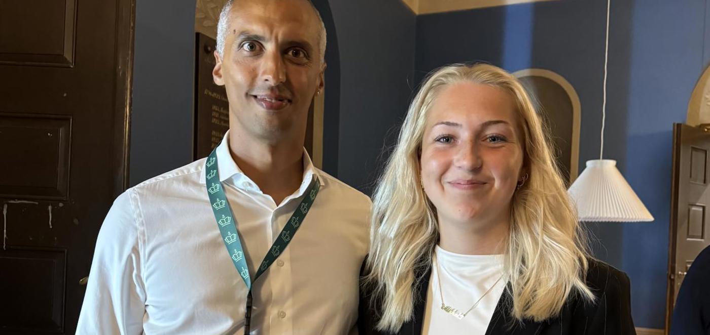 Mand i hvid skjorte med id-bånd og ung kvinde i sort vest står side om side og smiler