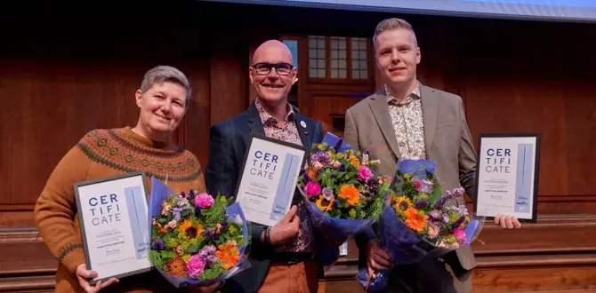 Tre personer står på en scene med certifikater og farverige blomsterbuketter