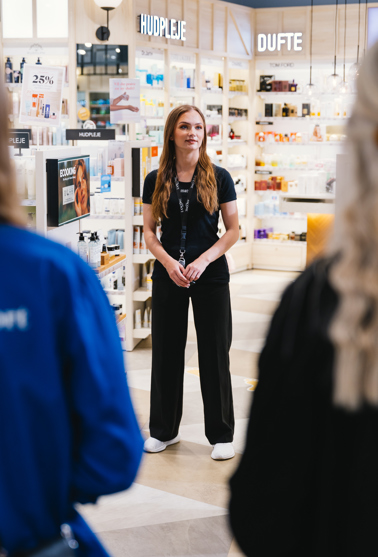 Medarbejder i sort uniform taler med kunder i en butik med hudpleje- og skønhedsprodukter