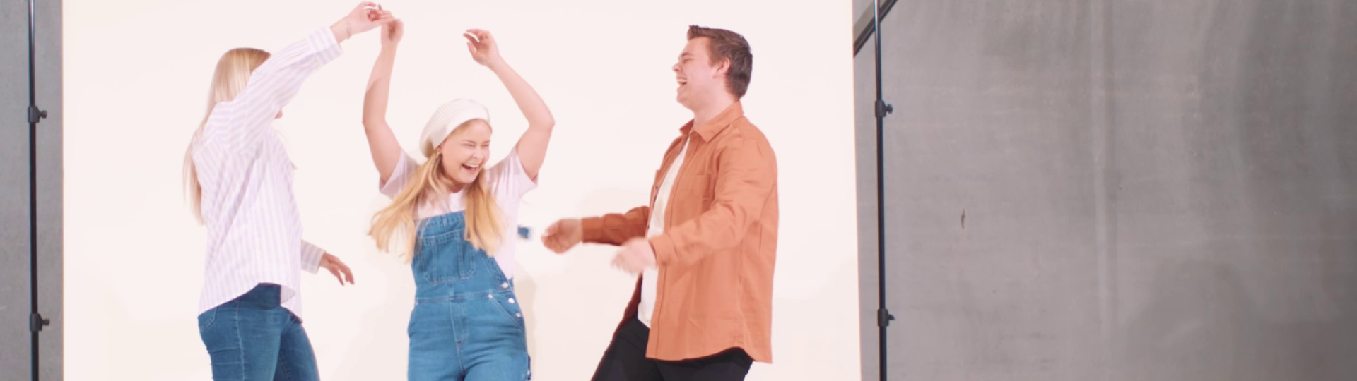 Tre unge mennesker danser og bevæger sig gladeligt foran en lys baggrund