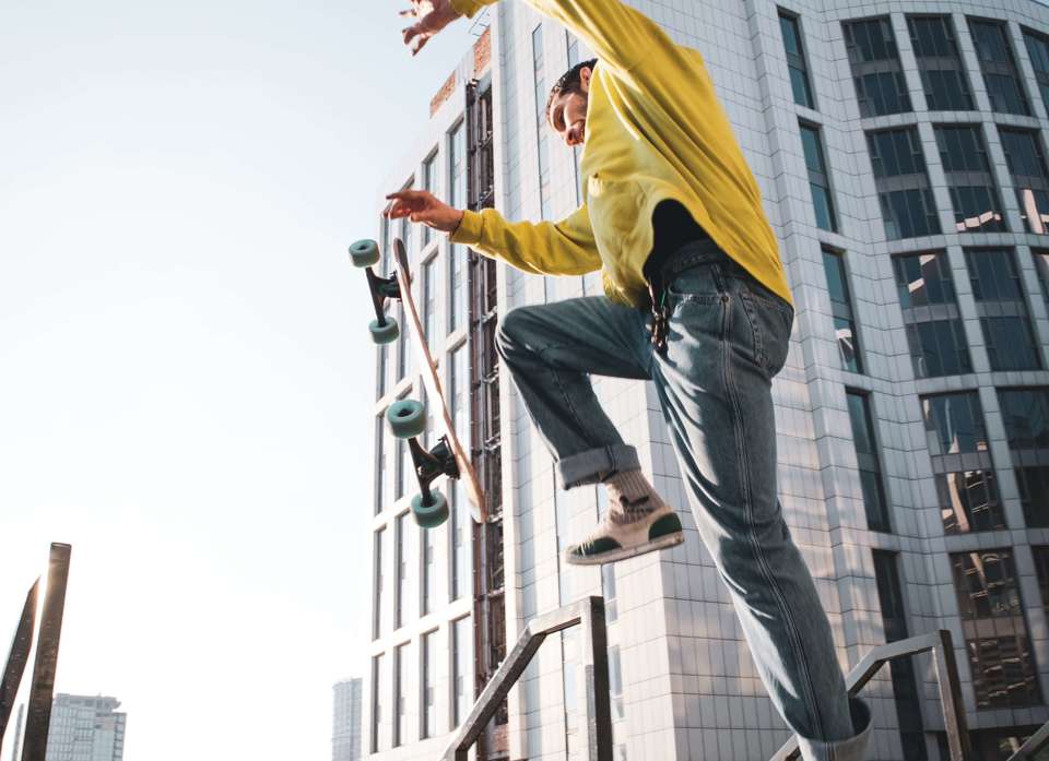 Ung person med skateboard springer over trappeskillerum foran moderne bygning