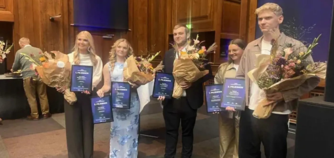 Fem unge står på række med diplomer og blomsterbuketter ved en prisuddeling