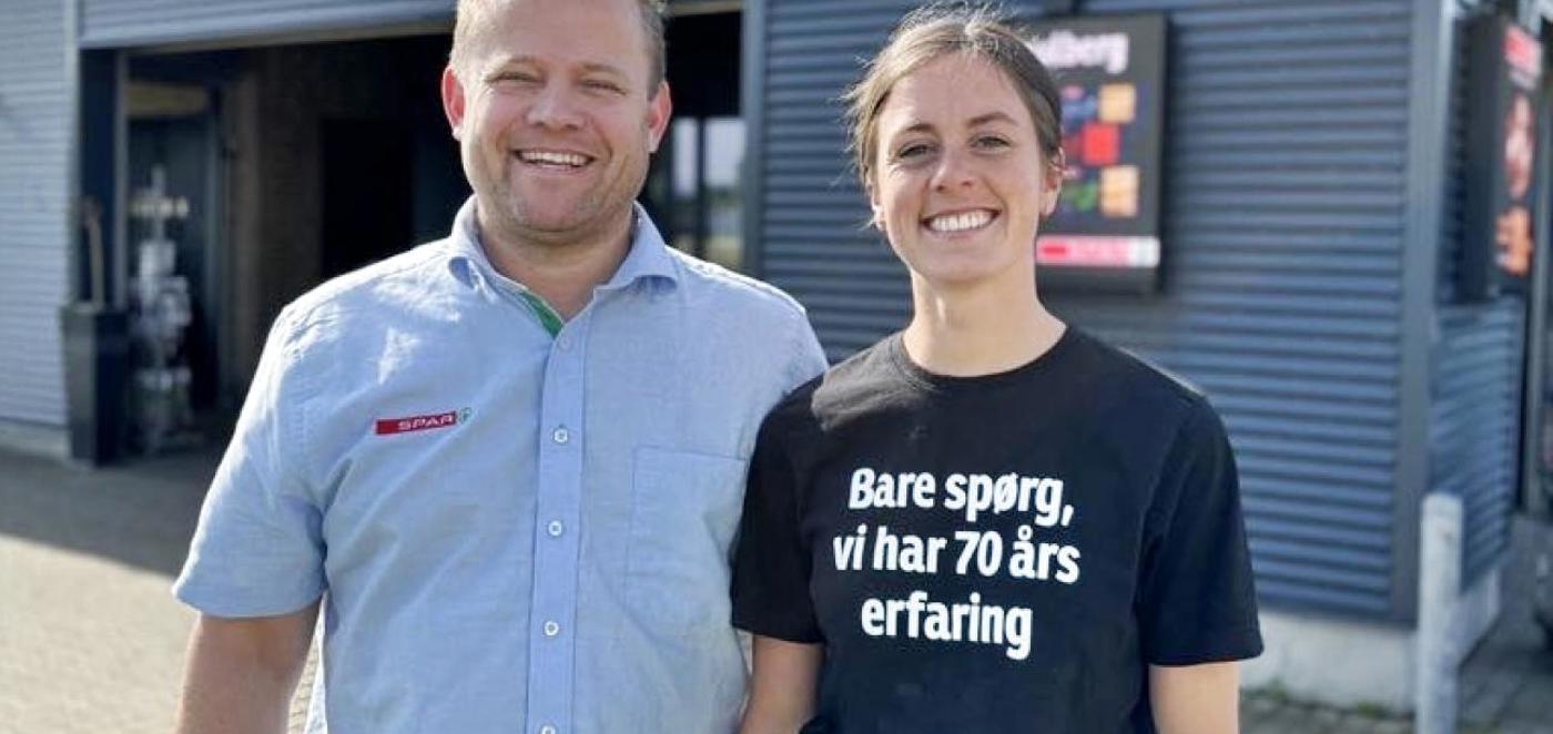 En mandlig og en kvindelig medarbejder i Spar-uniform står foran en supermarkedsindgang og smiler