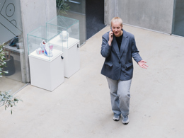 Ung kvinde i jakkesæt taler i telefon mens hun går gennem moderne bygning med udstillingsvitrine