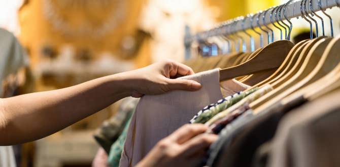 Hænder bladrer gennem tøj på bøjler i en butik
