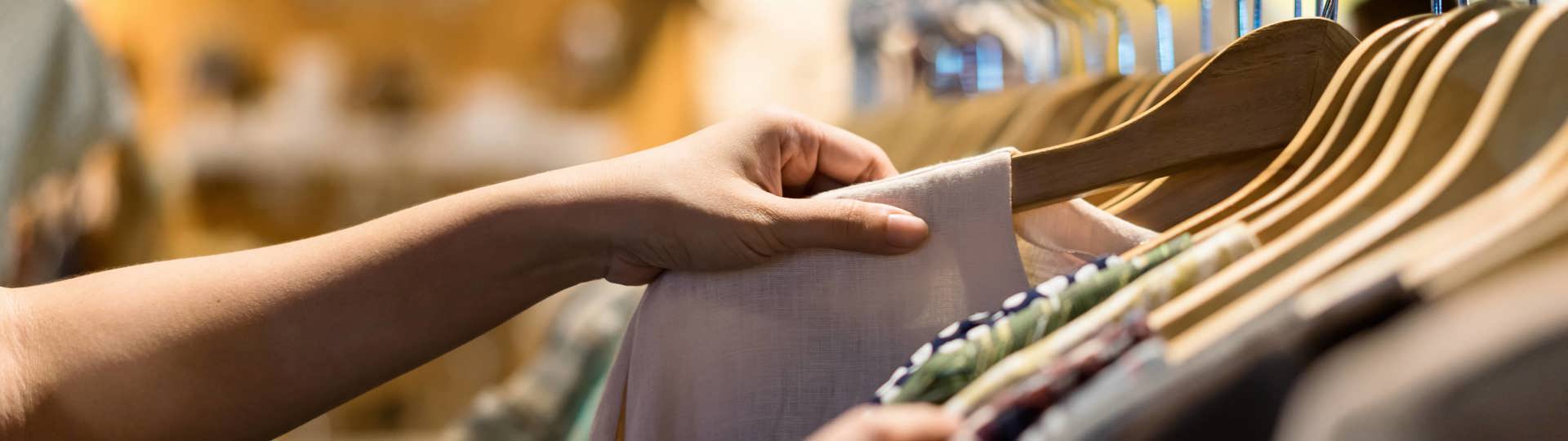 Hænder bladrer gennem tøj på bøjler i en butik