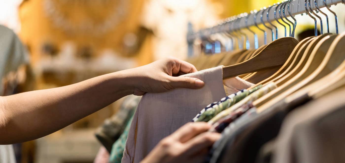 Hænder bladrer gennem tøj på bøjler i en butik