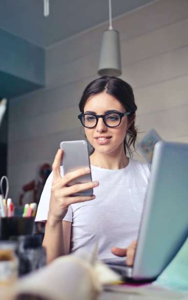 Ung kvinde med briller sidder ved skrivebord med laptop og smartphone